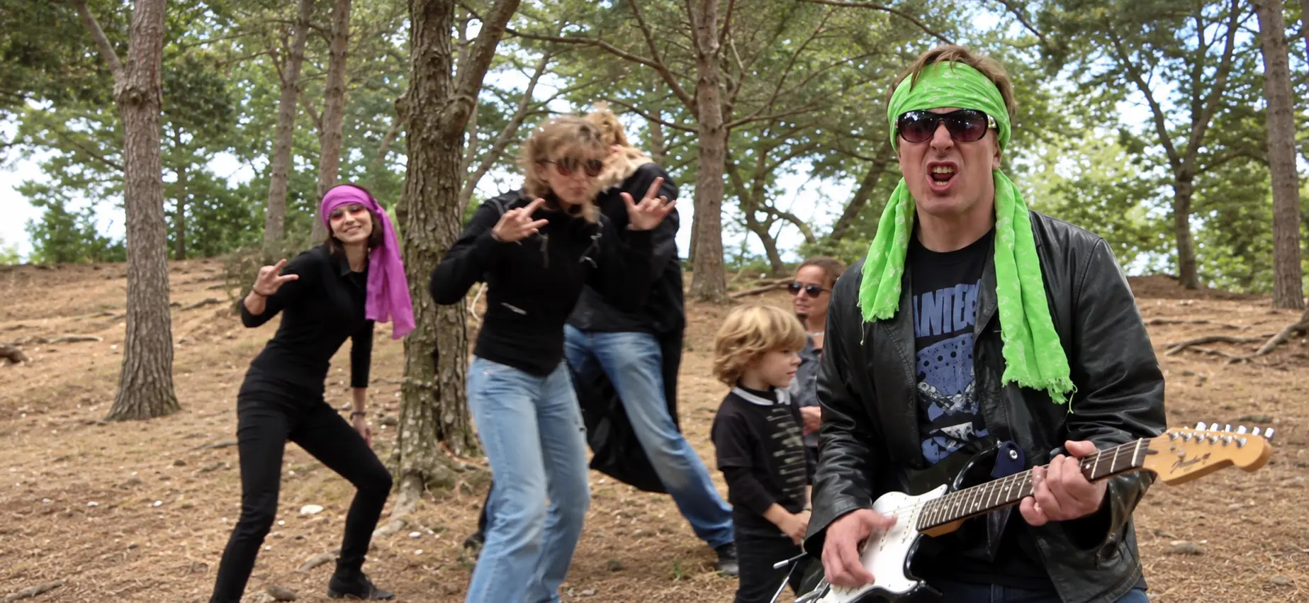 Participante con guitarra y pañuelo verde en una escena de videoclip de cumpleaños al aire libre